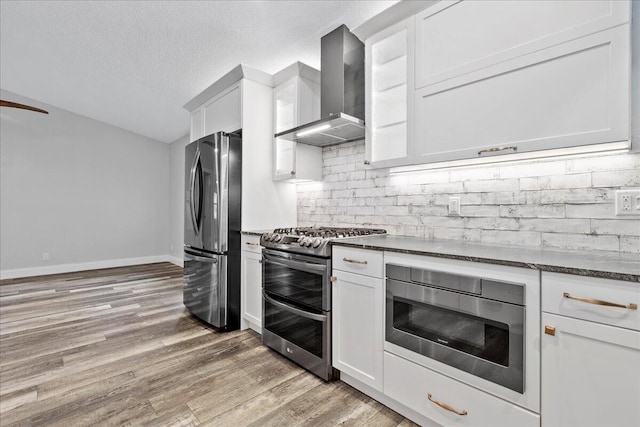 kitchen featuring appliances with stainless steel finishes, dark hardwood / wood-style flooring, wall chimney range hood, and white cabinetry