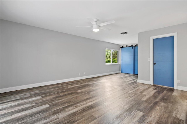 empty room with ceiling fan, a barn door, and dark hardwood / wood-style floors