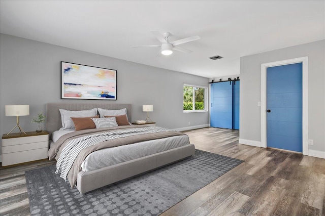 bedroom with a barn door, wood-type flooring, and ceiling fan