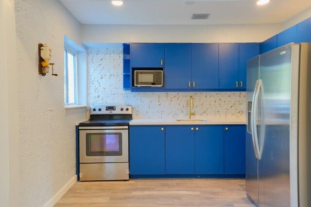 kitchen featuring light wood-type flooring, appliances with stainless steel finishes, blue cabinetry, and sink