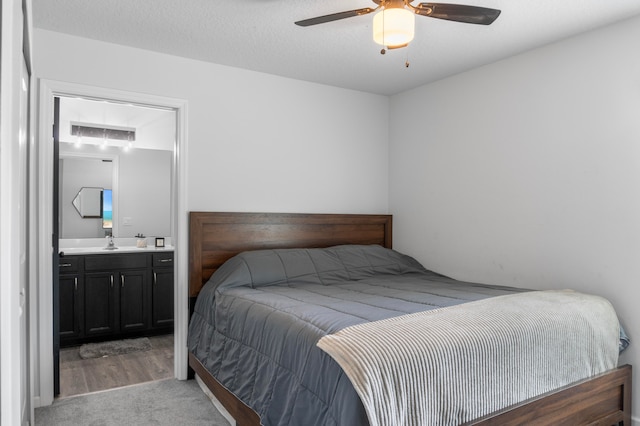 bedroom with light wood-type flooring, a textured ceiling, sink, ensuite bathroom, and ceiling fan