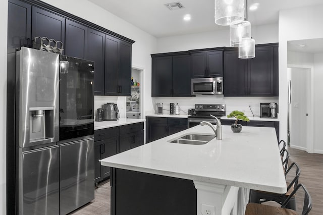 kitchen featuring a breakfast bar, sink, an island with sink, hanging light fixtures, and stainless steel appliances