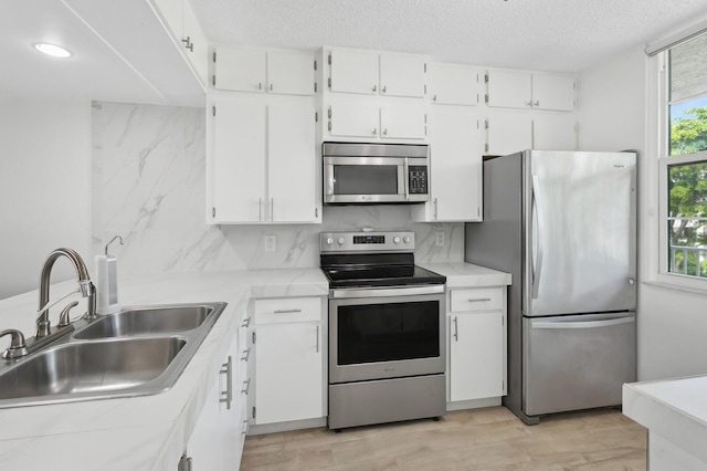 kitchen with backsplash, stainless steel appliances, white cabinetry, and sink