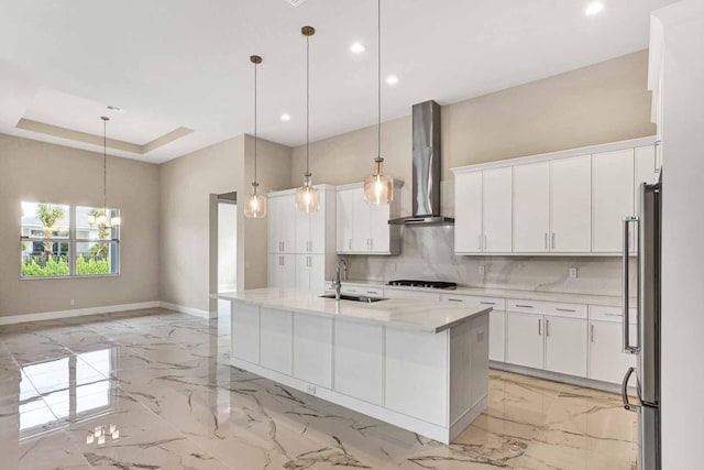 kitchen featuring white cabinets, an island with sink, wall chimney exhaust hood, decorative light fixtures, and sink