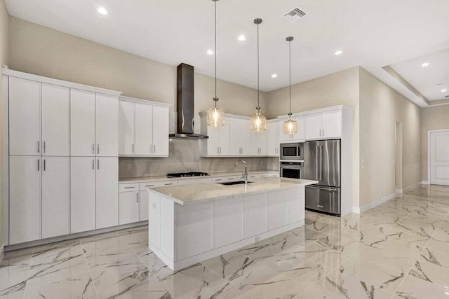 kitchen featuring white cabinetry, a kitchen island with sink, pendant lighting, wall chimney exhaust hood, and stainless steel appliances