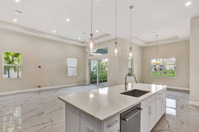 kitchen featuring hanging light fixtures, a tray ceiling, a center island with sink, sink, and white cabinetry