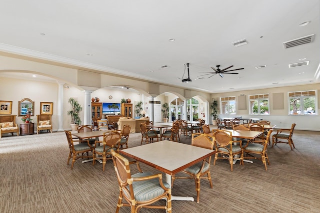 carpeted dining space featuring ceiling fan, crown molding, and decorative columns