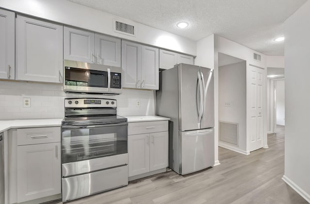 kitchen with gray cabinetry, a textured ceiling, backsplash, stainless steel appliances, and light hardwood / wood-style floors