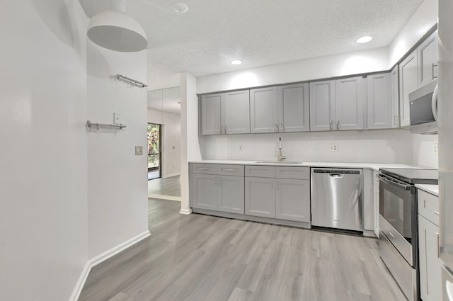 kitchen featuring gray cabinetry, light hardwood / wood-style floors, stainless steel appliances, a textured ceiling, and sink