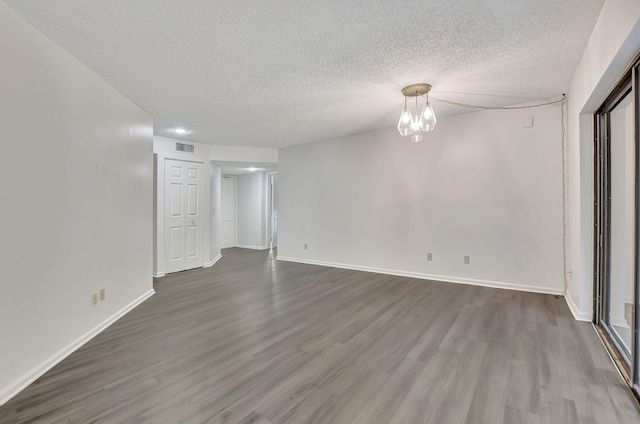 unfurnished room with a textured ceiling, hardwood / wood-style floors, and a notable chandelier