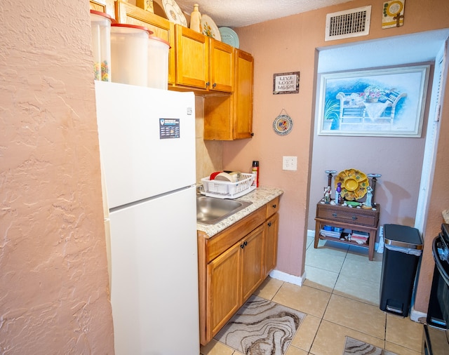 kitchen with a textured ceiling, light tile patterned flooring, white fridge, and sink