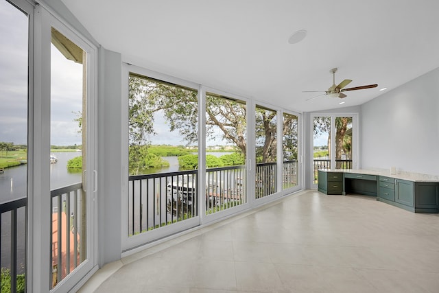 unfurnished sunroom featuring a water view, ceiling fan, and built in desk