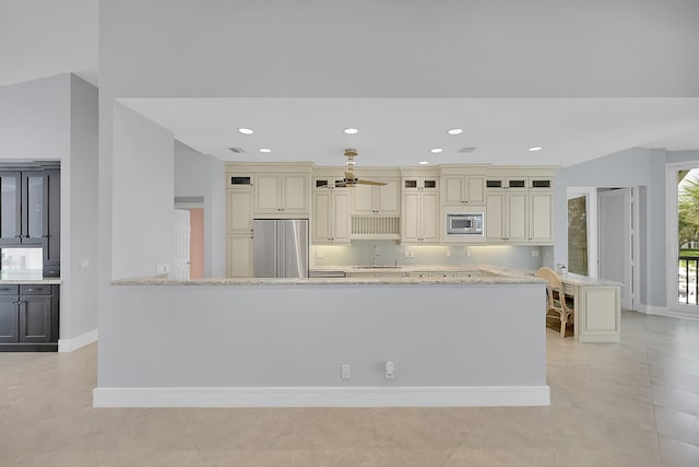 kitchen with light stone countertops, appliances with stainless steel finishes, cream cabinetry, and lofted ceiling