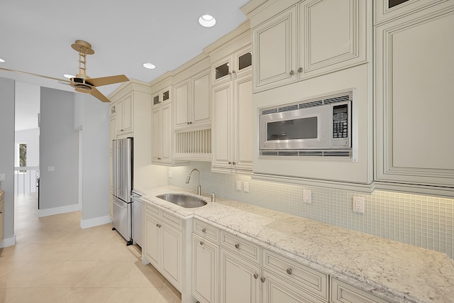 kitchen with cream cabinetry, sink, light stone counters, stainless steel appliances, and backsplash