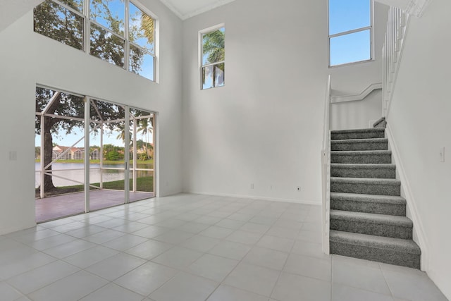 unfurnished living room with crown molding, light tile patterned flooring, and a high ceiling