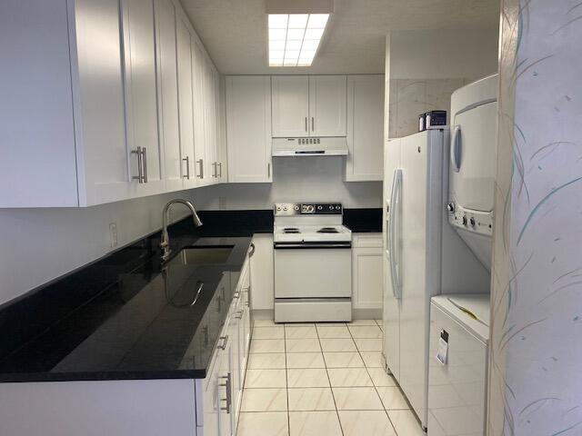 kitchen featuring light tile patterned floors, sink, white appliances, white cabinetry, and stacked washer and dryer