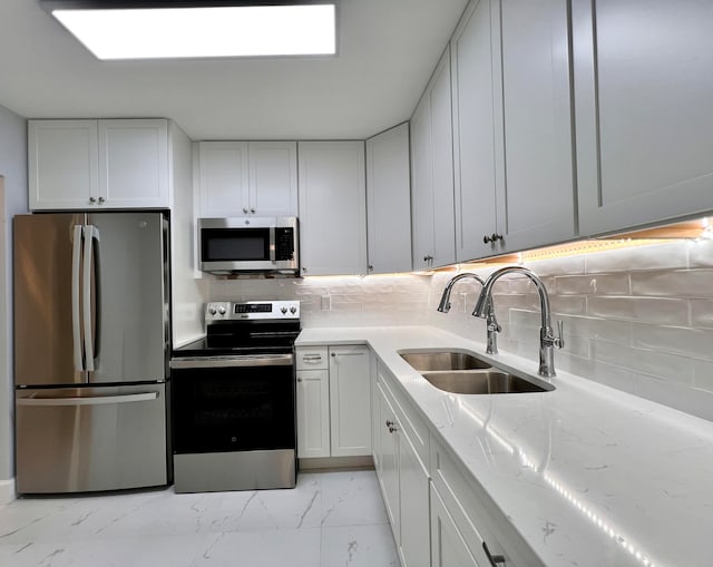 kitchen with white cabinets, sink, backsplash, appliances with stainless steel finishes, and light stone countertops