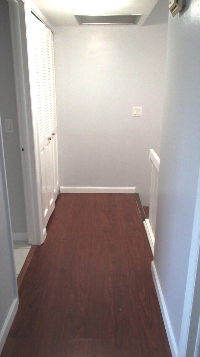 hallway with dark wood-type flooring, an upstairs landing, and baseboards