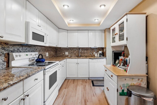 kitchen with white appliances, white cabinets, a raised ceiling, sink, and light hardwood / wood-style floors