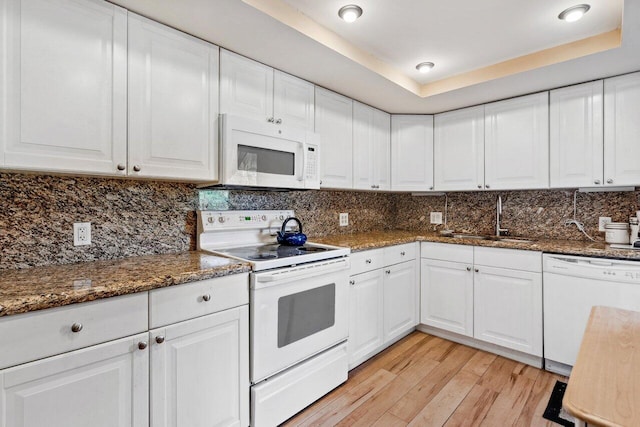 kitchen with white appliances, white cabinets, sink, light wood-type flooring, and a tray ceiling