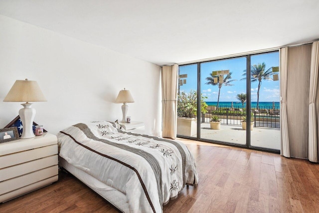 bedroom with expansive windows, access to outside, hardwood / wood-style flooring, and a water view