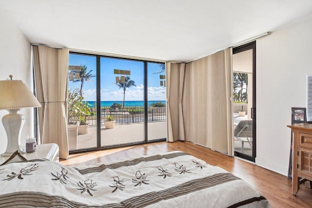 bedroom with access to outside, a water view, expansive windows, and light hardwood / wood-style floors