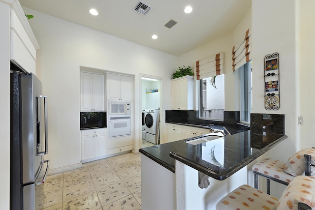 kitchen with a breakfast bar, white appliances, white cabinetry, washing machine and clothes dryer, and backsplash