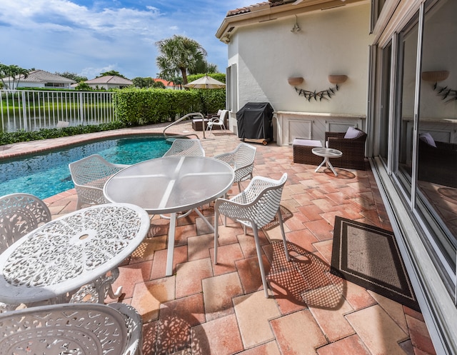 view of swimming pool with a water view, a grill, and a patio area