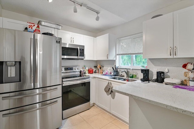 kitchen with white cabinets, appliances with stainless steel finishes, light stone counters, and track lighting