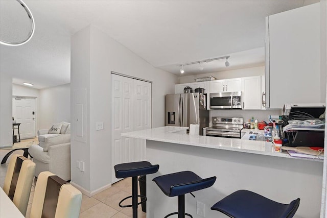 kitchen featuring light stone counters, lofted ceiling, kitchen peninsula, white cabinets, and appliances with stainless steel finishes