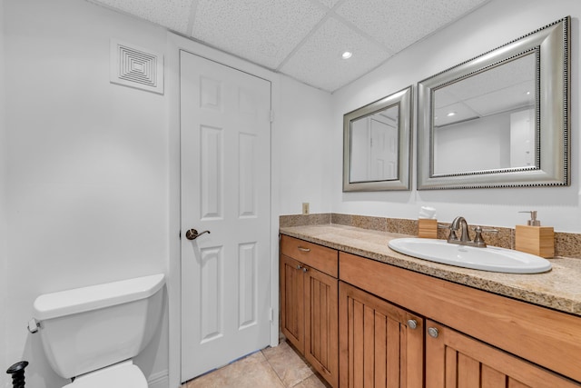 bathroom with a paneled ceiling, vanity, toilet, and tile patterned flooring