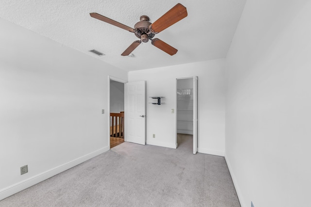 unfurnished bedroom featuring a spacious closet, light carpet, a textured ceiling, a closet, and ceiling fan