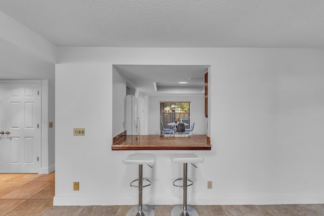 kitchen featuring a tray ceiling, a kitchen breakfast bar, white fridge with ice dispenser, light tile patterned floors, and kitchen peninsula