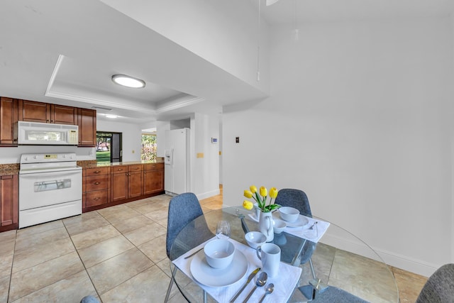 kitchen featuring a raised ceiling, light tile patterned flooring, light stone counters, and white appliances