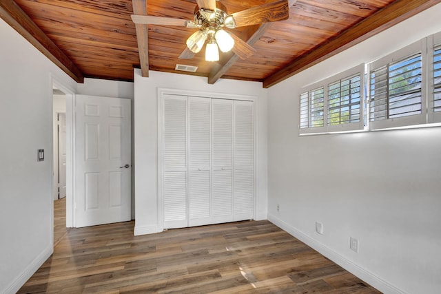 unfurnished bedroom featuring dark hardwood / wood-style floors, wooden ceiling, beam ceiling, and a closet