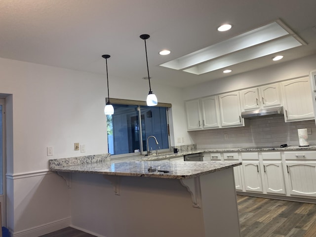 kitchen with pendant lighting, white cabinets, sink, a kitchen bar, and kitchen peninsula