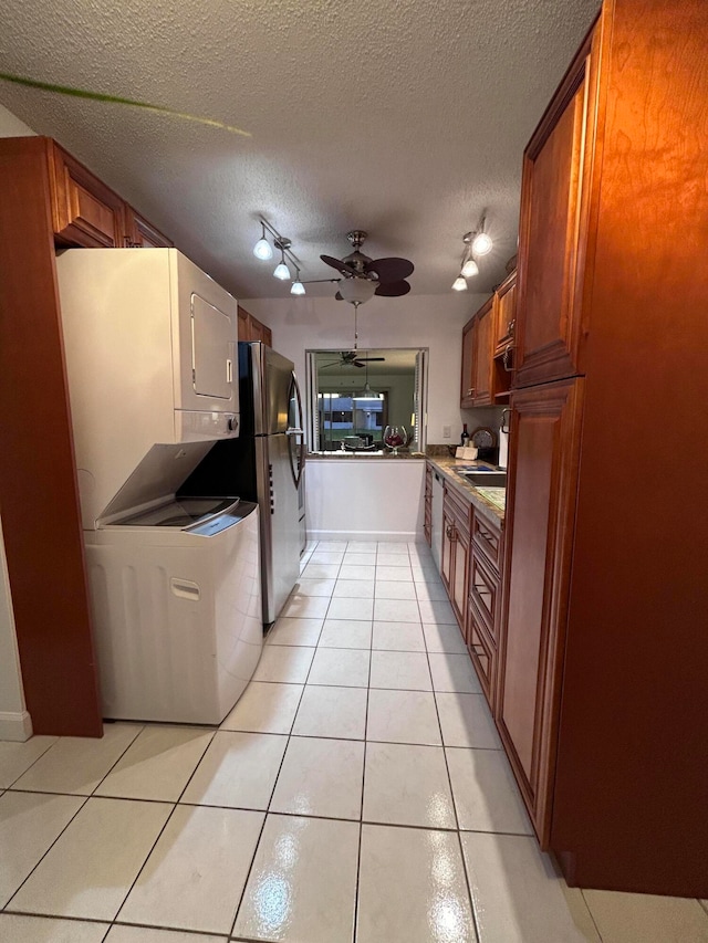 kitchen featuring a textured ceiling, ceiling fan, light tile patterned floors, stainless steel refrigerator, and stacked washer / drying machine