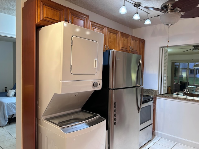 kitchen featuring stainless steel appliances, light tile patterned floors, stacked washing maching and dryer, and a textured ceiling