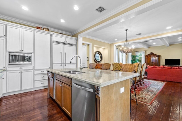 kitchen with stainless steel appliances, a center island with sink, sink, light stone countertops, and white cabinetry