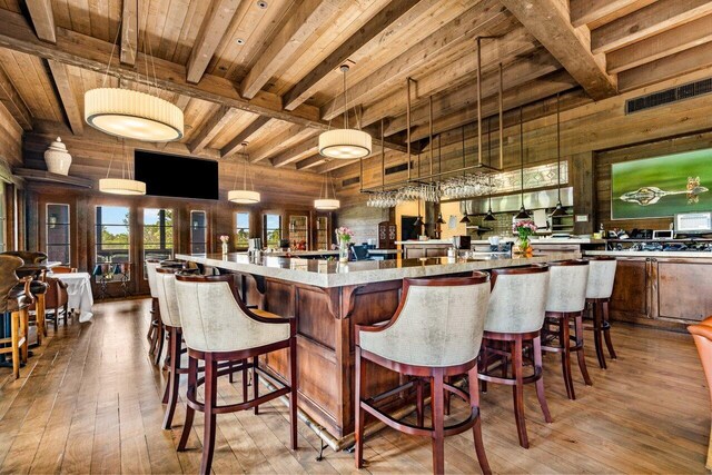 bar featuring wood walls, light hardwood / wood-style floors, beamed ceiling, decorative light fixtures, and wood ceiling