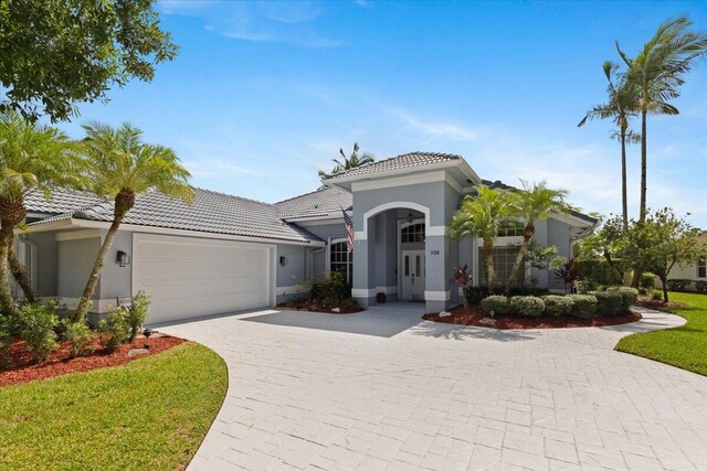 mediterranean / spanish home featuring a front lawn, a tiled roof, a garage, stucco siding, and decorative driveway