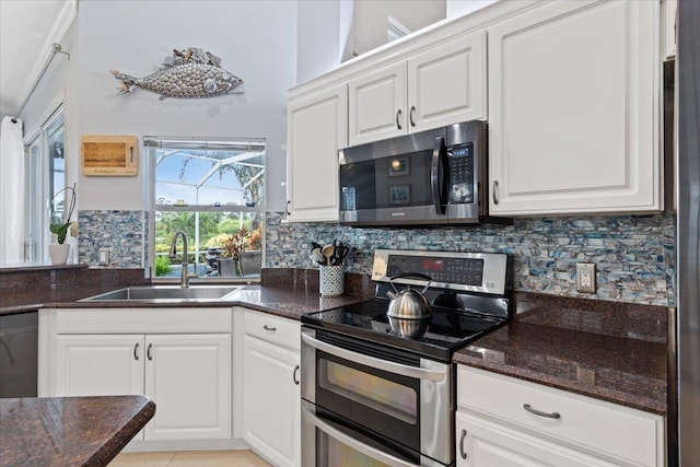 kitchen featuring dark stone countertops, a sink, decorative backsplash, stainless steel appliances, and white cabinets
