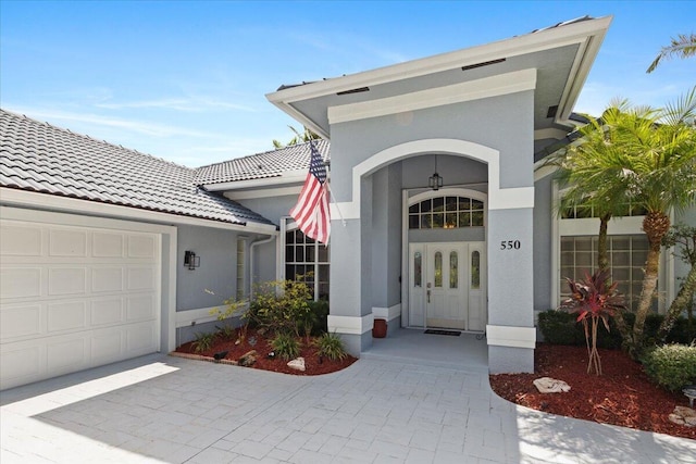 doorway to property featuring an attached garage, a tiled roof, and stucco siding