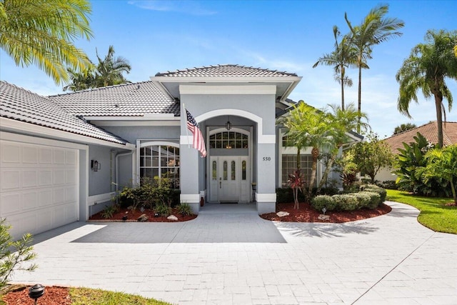 view of exterior entry with stucco siding, an attached garage, driveway, and a tile roof