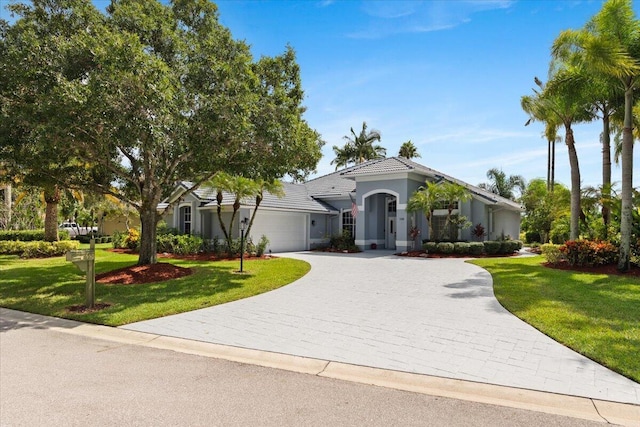 view of front of house with a tile roof, decorative driveway, a front lawn, and a garage