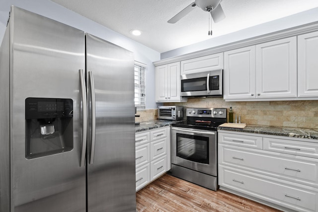 kitchen featuring ceiling fan, white cabinets, light hardwood / wood-style flooring, stainless steel appliances, and dark stone countertops