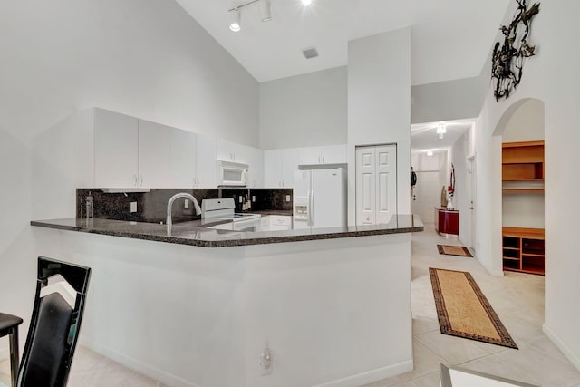 kitchen featuring a high ceiling, kitchen peninsula, white appliances, and light tile patterned floors