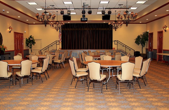 carpeted dining area with ornamental molding, a chandelier, and a paneled ceiling