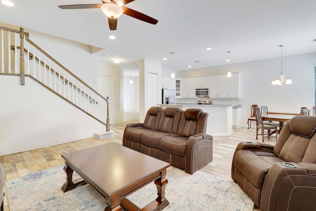 living room featuring ceiling fan with notable chandelier and light wood-type flooring