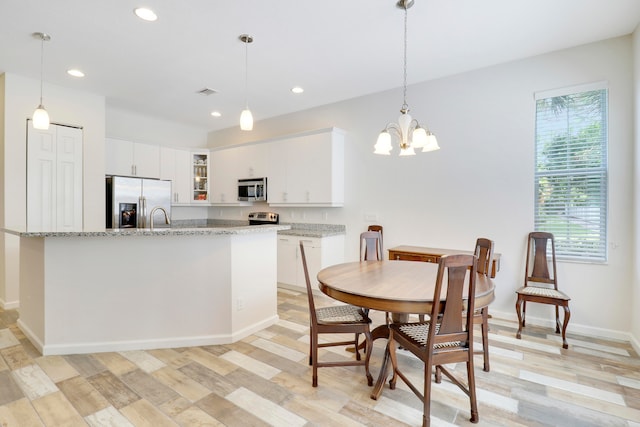 kitchen featuring white cabinets, light stone counters, appliances with stainless steel finishes, and an inviting chandelier